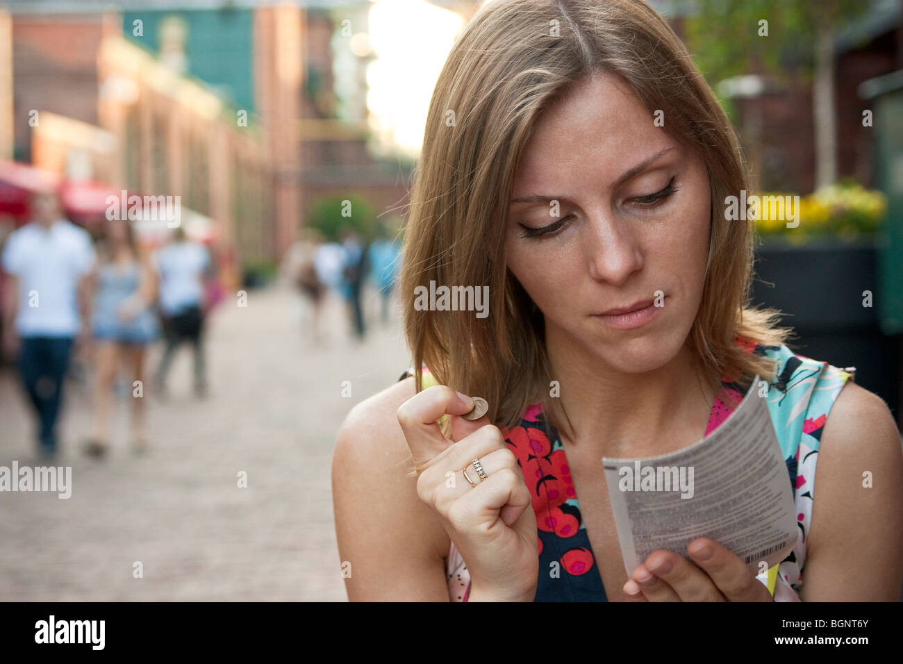 Jeune femme jouant une loterie à gratter, tenant une pièce de monnaie Banque D'Images