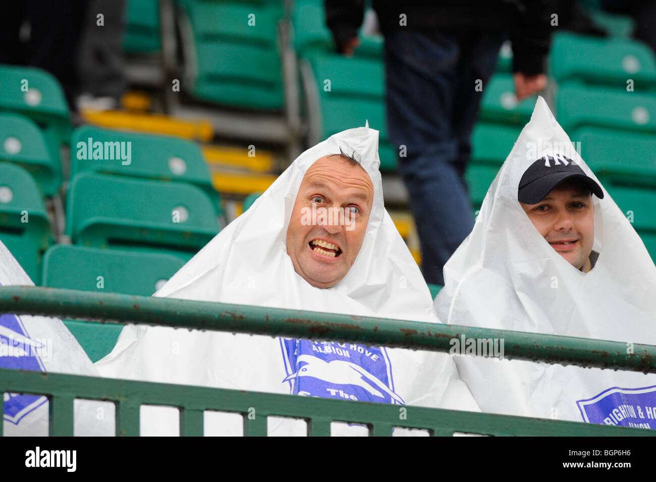 Forte pluie voit ces deux supporters portant des sacs en plastique en forme de pyramide à garder au sec à Brighton. Banque D'Images