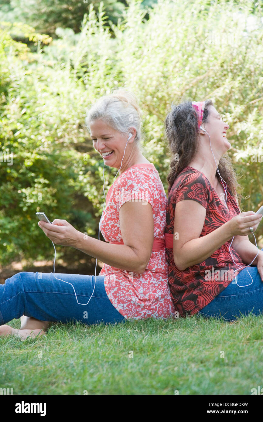 Profil de côté deux femmes d'âge mûr assis dos à dos dans un parc et à l'écoute de lecteurs MP3 Banque D'Images