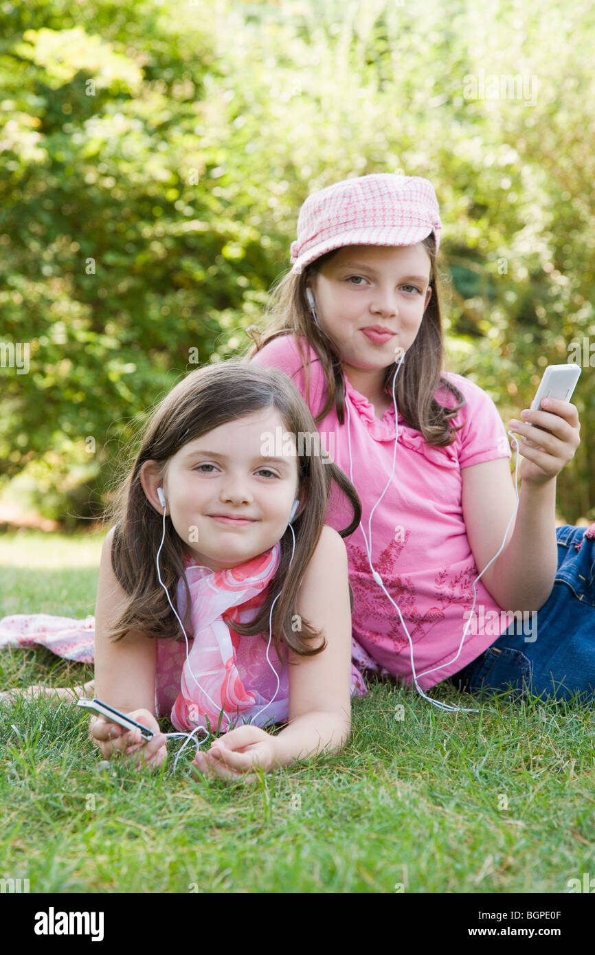 Portrait de deux sœurs à l'écoute de lecteurs MP3 dans un parc Banque D'Images