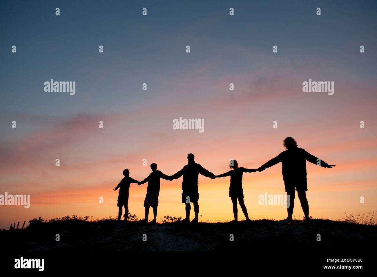 Le lien entre les mains une famille silhouetté contre un coucher du soleil à Le Guilvinec, Bretagne Sud, France Banque D'Images