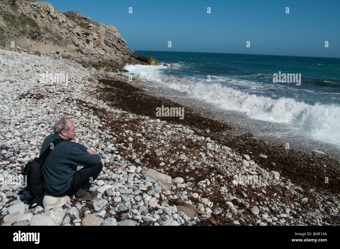 Homme assis sur plage en regardant les vagues, Ladram Bay, Devon Banque D'Images