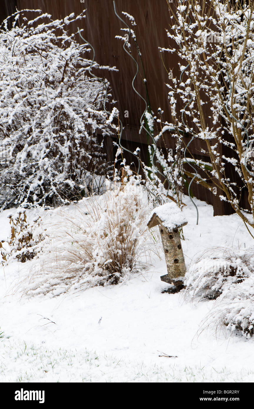 Jardin anglais frontière avec coccinelle maison et graminées ornementales dans la neige Banque D'Images