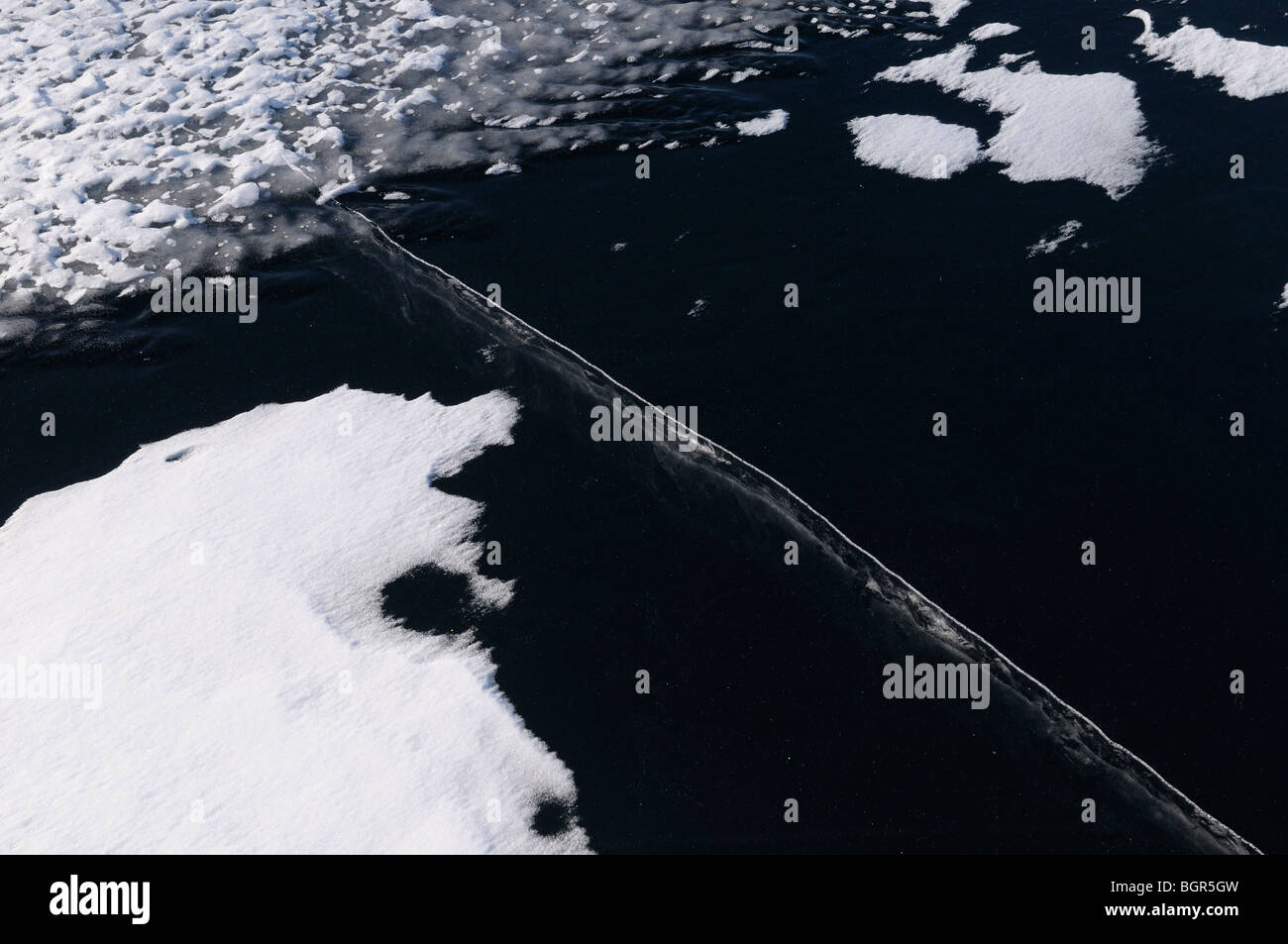 Glace noire sur un lac avec une grande fissure profonde et de surface ondulée et des amoncellements de neige Banque D'Images