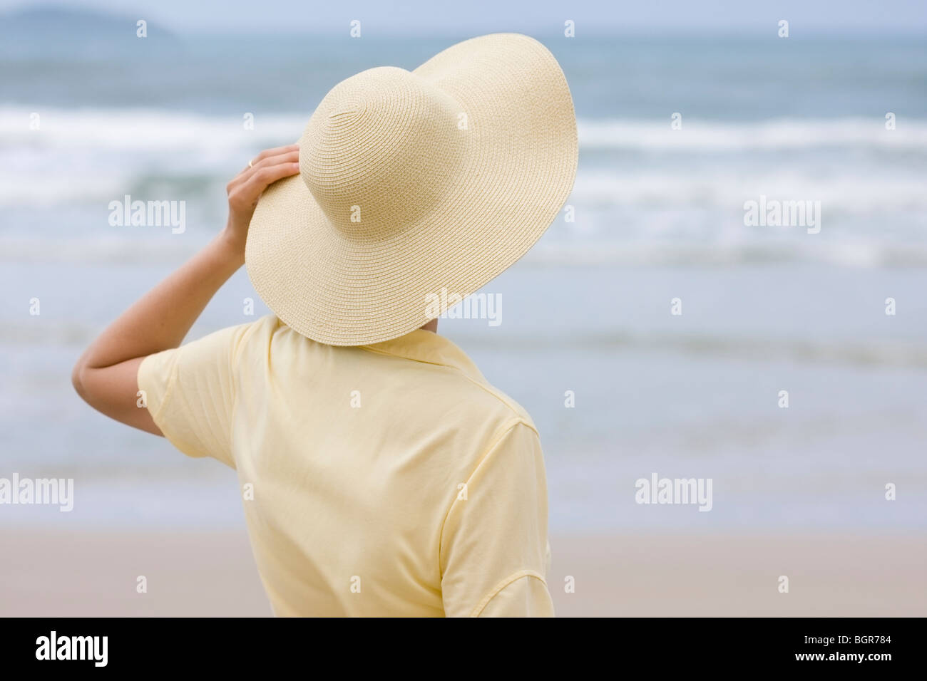 Femme avec chapeau jaune et shirt face à la mer - se concentrer sur l'hat Banque D'Images