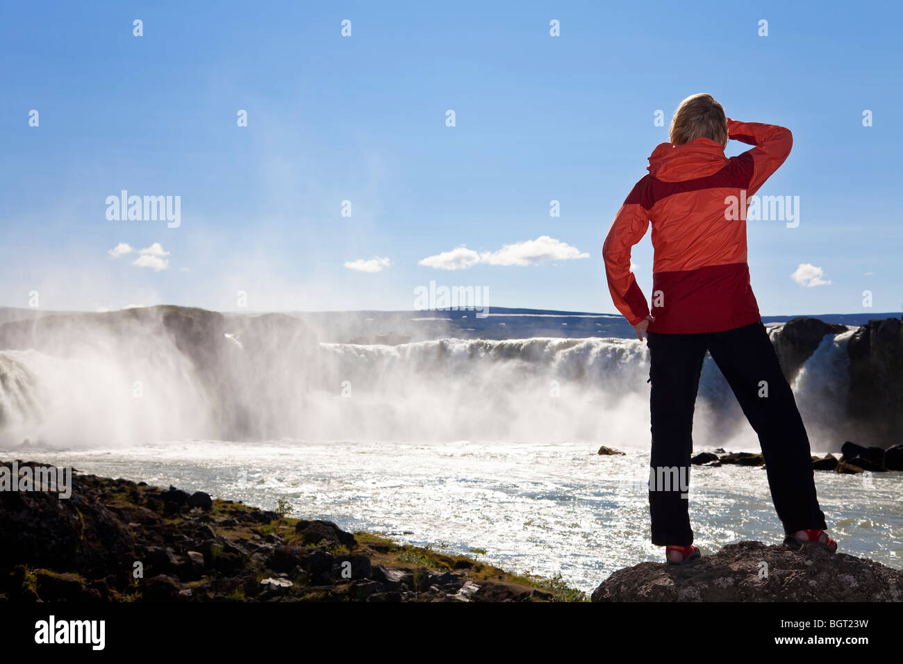Une femme de randonneur explorer tourné en golden lumière du soir en face d'une immense cascade. Sur l'emplacement à cascade Godafoss, Islande. Banque D'Images