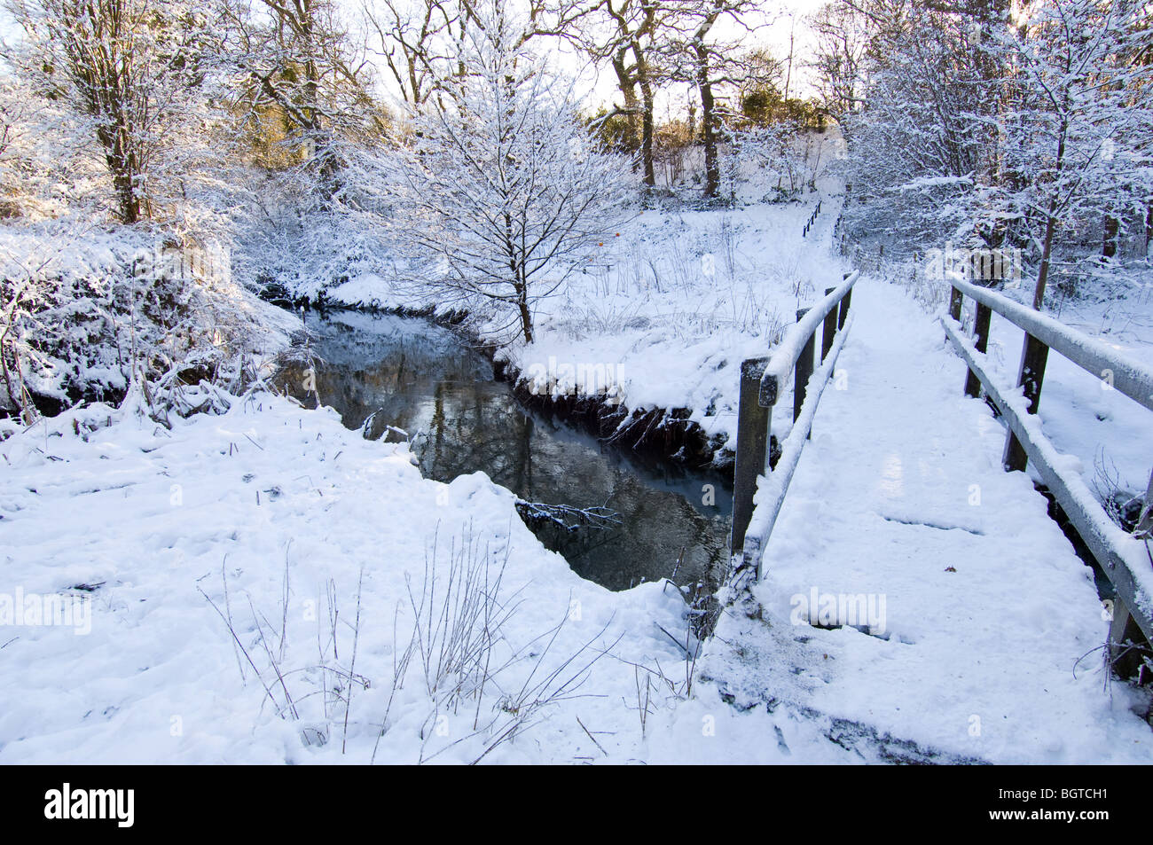 Un pont en bois de fortune en prenant un sentier sur une petite rivière pendant l'hiver avec de la neige au sol. Banque D'Images