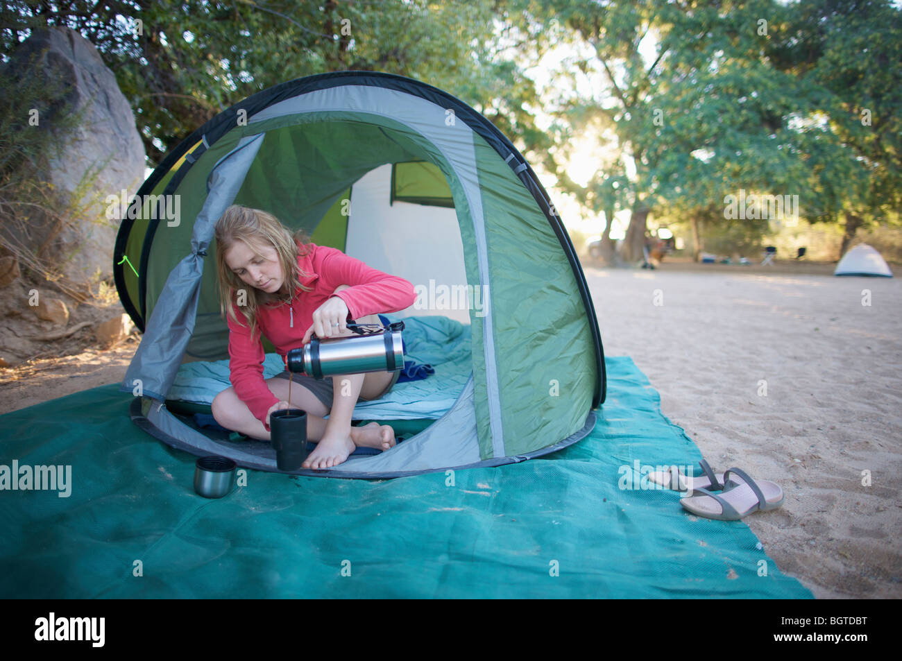 Young woman relaxing in tent versant une tasse de café, Van Zyl Col', Kaokoland, Namibie Banque D'Images