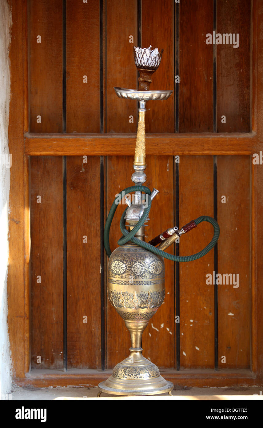 Un vieux narguilé ou shisha pipe avec un bol en laiton sur une fenêtre-cill avec un volet en bois derrière, dans le souk Waqif, Doha, Qatar Banque D'Images