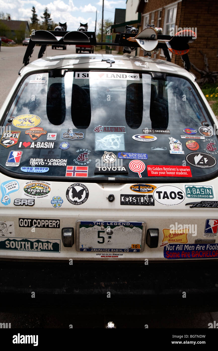 Vue arrière d'une petite voiture blanche Toyota avec de nombreux badges et autocollants et skis sur barre de toit - retirer la plaque de licence Banque D'Images