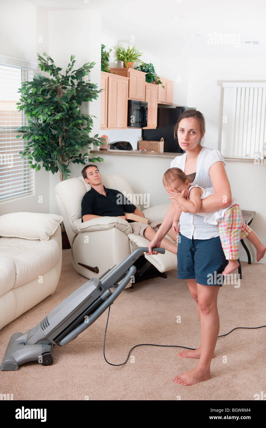 Une mère essayant de passer l'aspirateur pendant que le père se situe autour de Banque D'Images