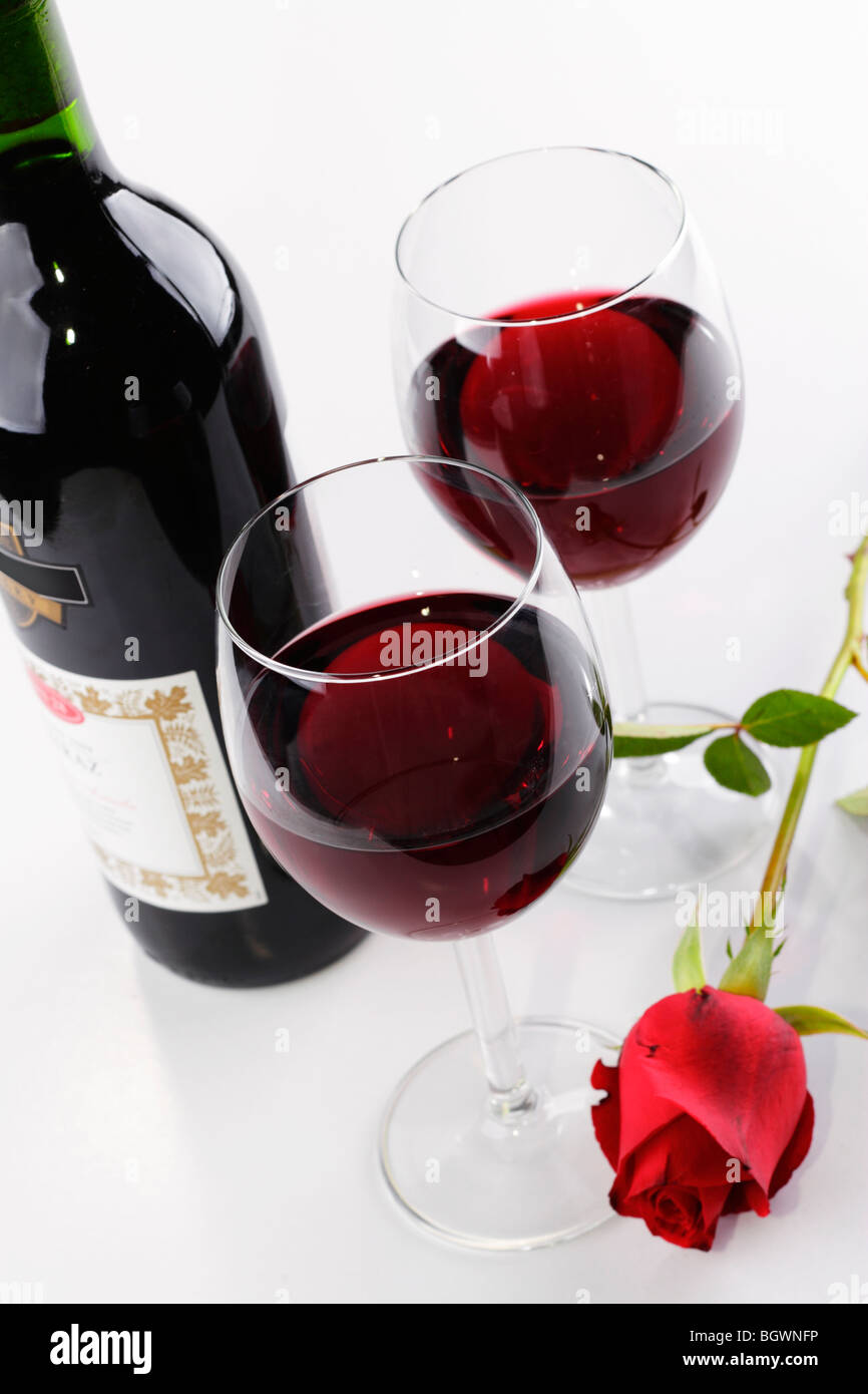 Une paire de verres de vin avec du vin rouge, une bouteille et une rose rouge Banque D'Images