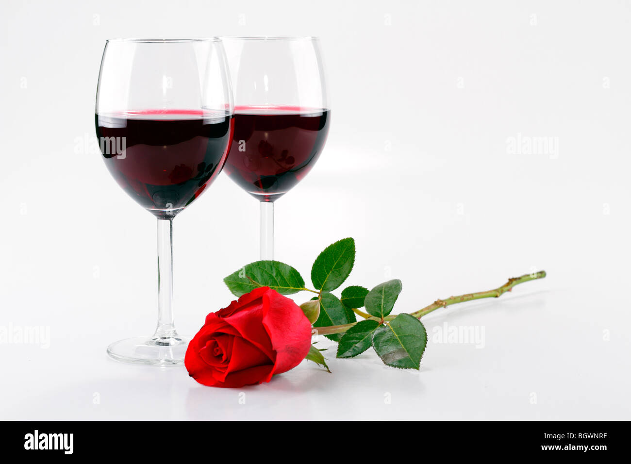 Une paire de verres de vin avec du vin rouge et une rose rouge Banque D'Images