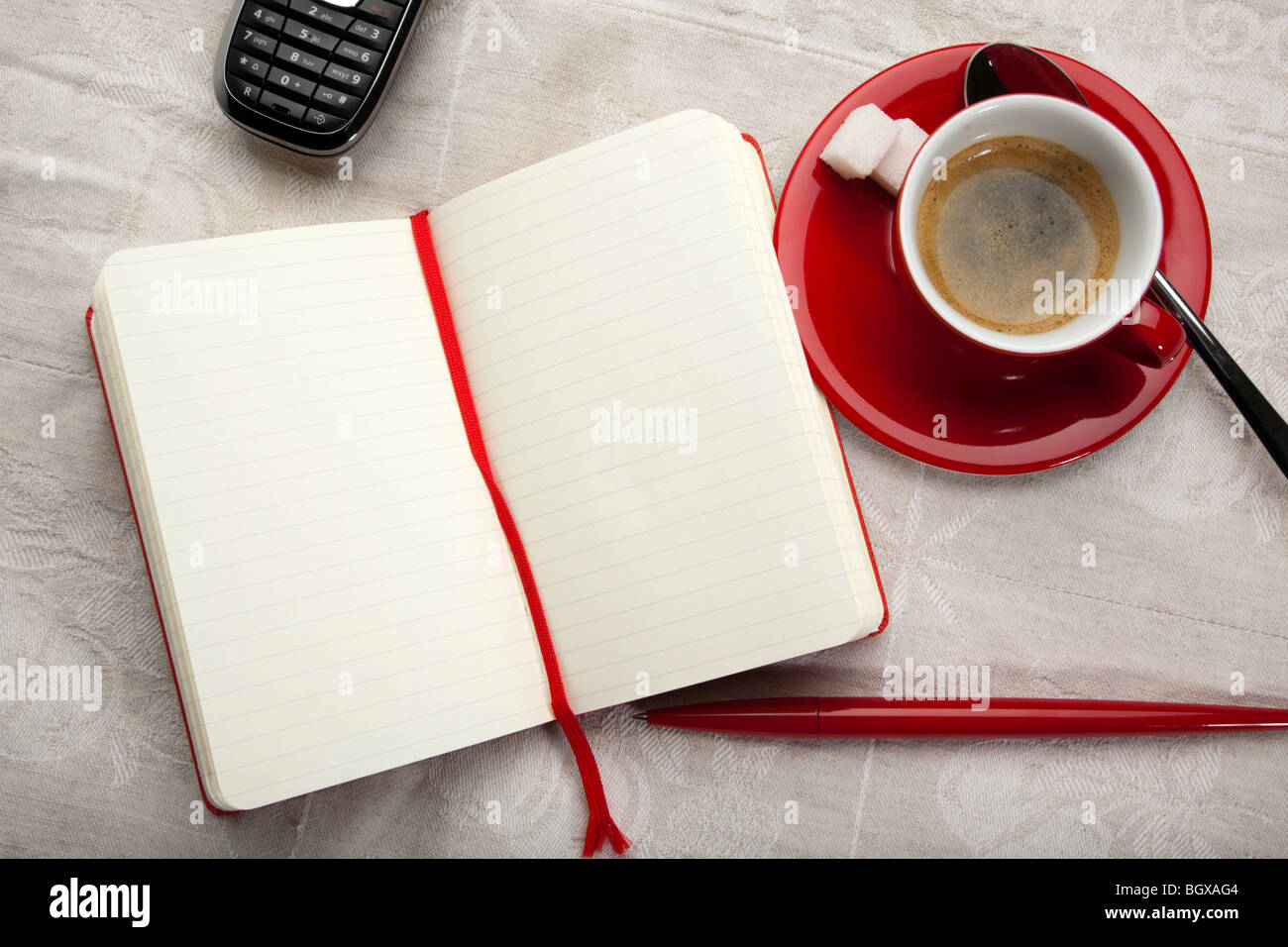 Ordinateur portable ouvert ou de journal avec des pages blanches, rouge tasse d'expresso, stylo à bille et d'un téléphone mobile sur table, voir les oiseaux Banque D'Images