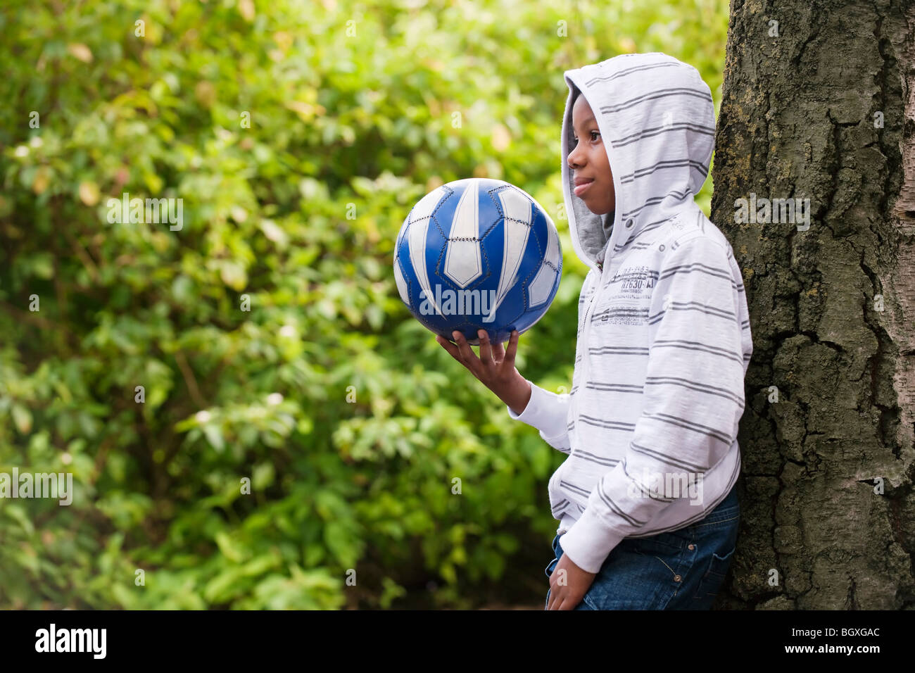 Boy leaning on tree with ball Banque D'Images