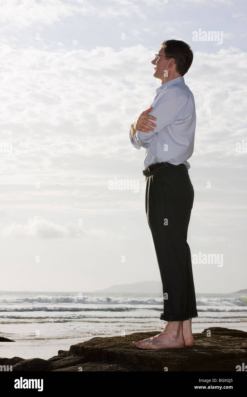 Businessman profitant du soleil sur un rocher sur une plage Banque D'Images