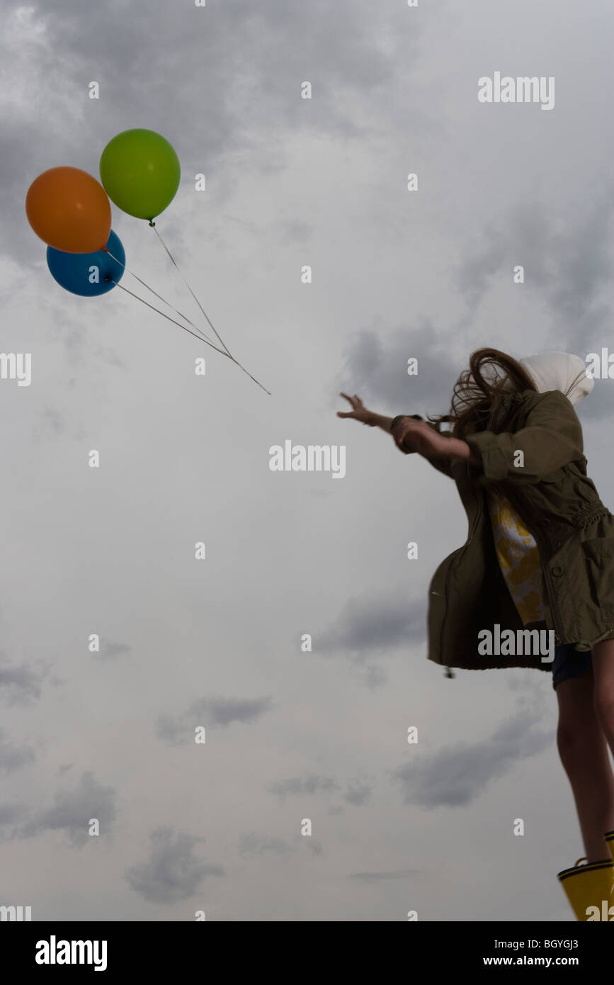 Femme regardant comme bouquet de ballons à flotter haut dans ciel nuageux Banque D'Images