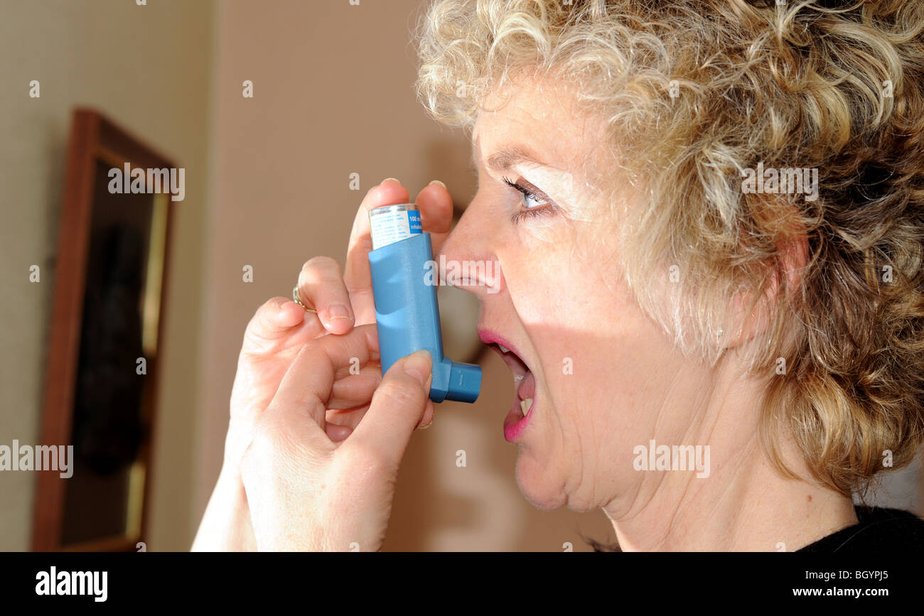 Femme à l'aide d'un inhalateur bleu pour aider avec son asthme le souffle court - posée par modèle Banque D'Images