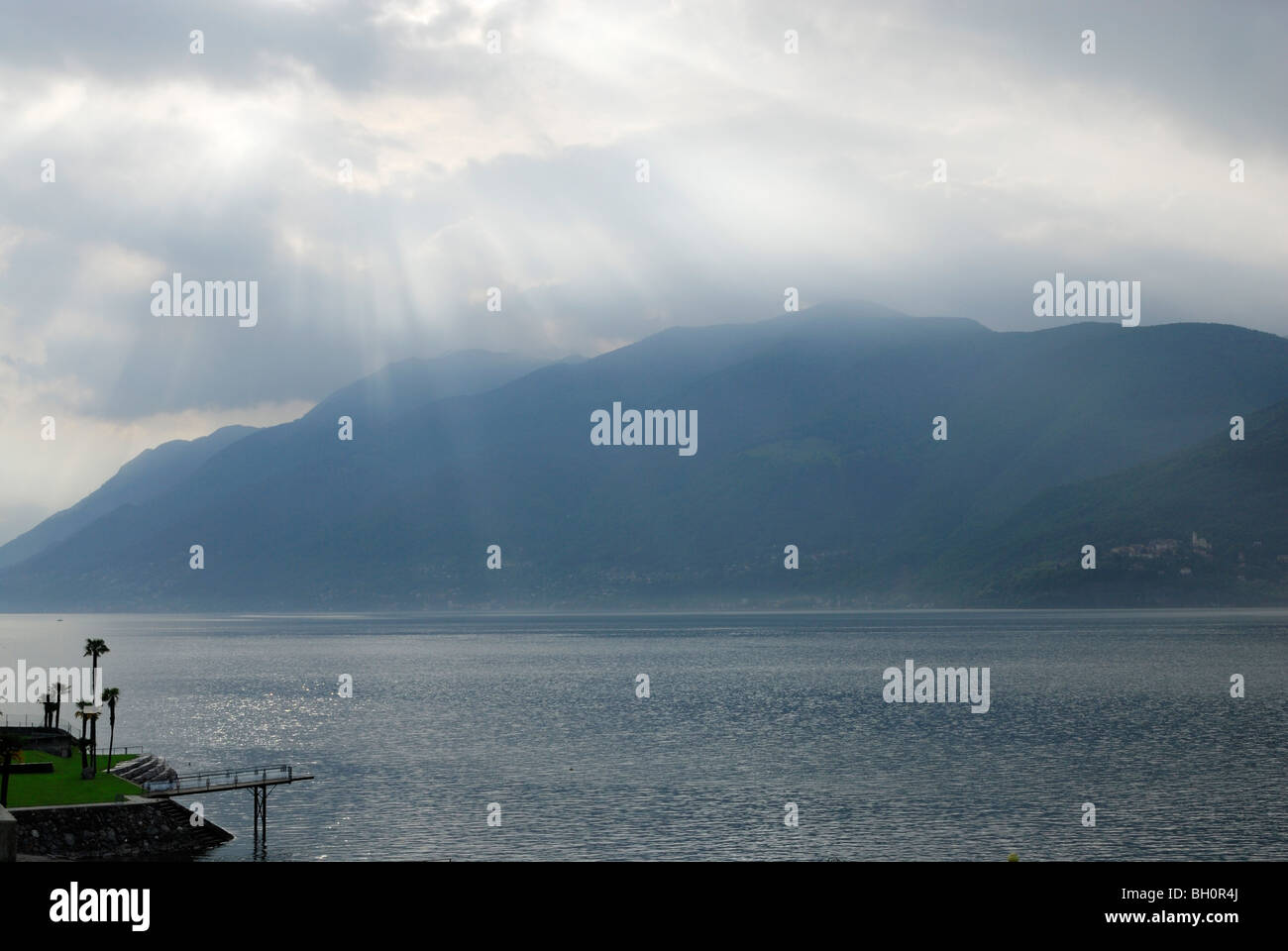 Rayons de soleil brillant à travers les nuages au-dessus du lac Majeur, un lido avec palmiers, Brissago, lac Majeur, Lac Majeur, Tessin, Banque D'Images