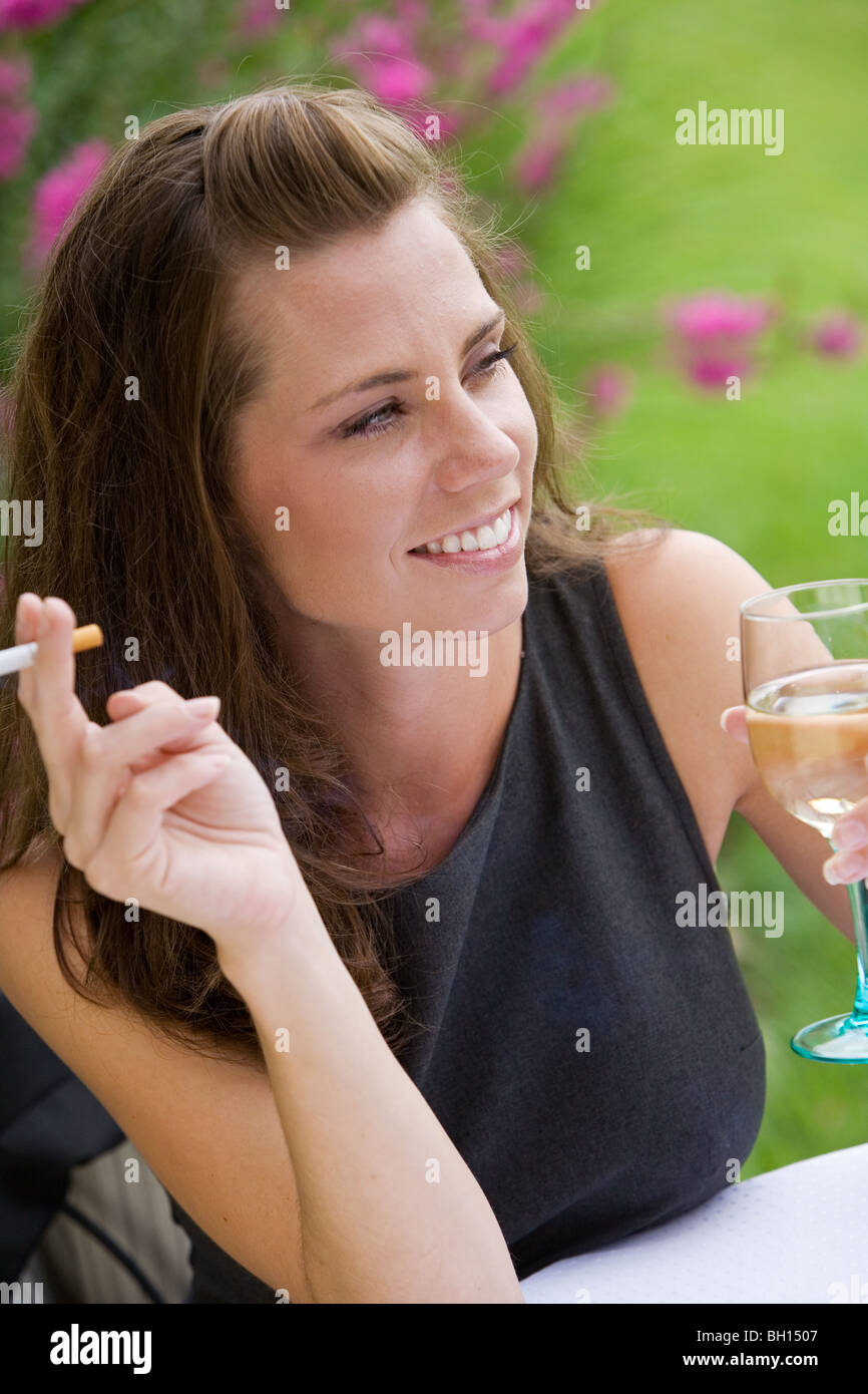 Jeune femme se détendre avec un verre de vin et une cigarette dans un café en plein air Banque D'Images