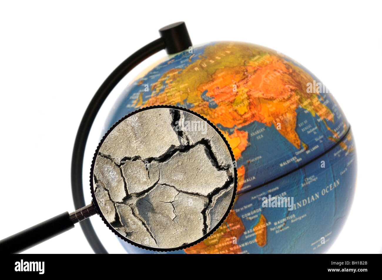 La terre craquelée par la sécheresse vu à travers une loupe tenu contre allumé globe terrestre Banque D'Images