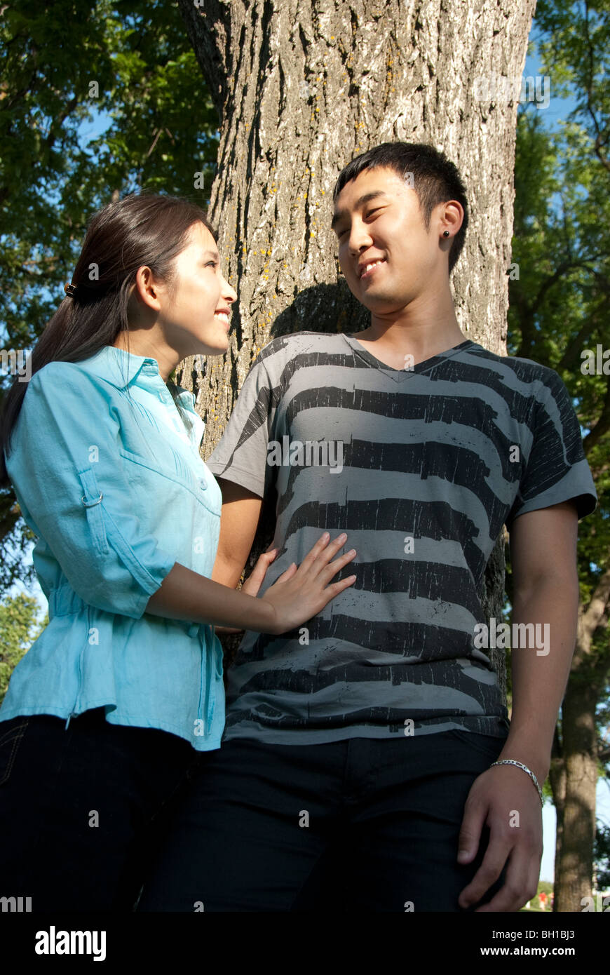 Jeune couple se placer à côté de l'arbre dans le parc Assiniboine, Winnipeg, Manitoba, Canada Banque D'Images