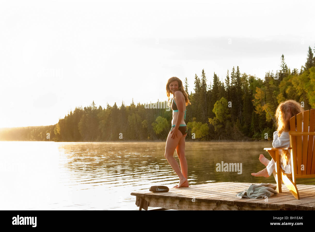 Femme debout en maillot, deuxième femme assise dans une chaise sur dock, Clear Lake, Manitoba, Canada Banque D'Images