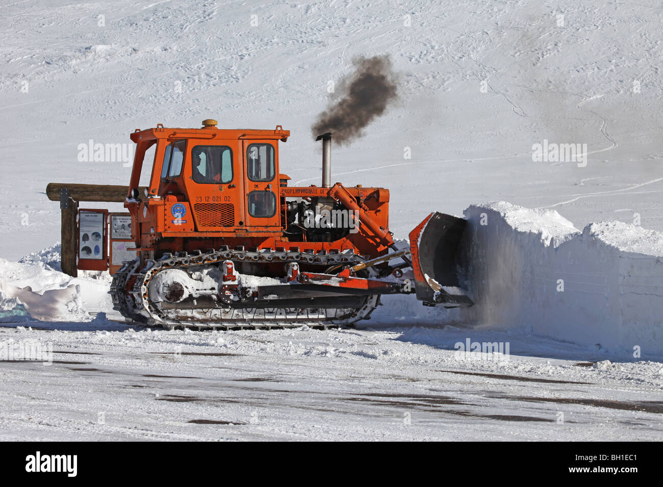 Caterpillar bulldozer poussant la neige profonde au large de route de montagne dans le centre de l'Utah. Véhicule de couleur orange avec moteur diesel. Pollution atmosphérique Banque D'Images