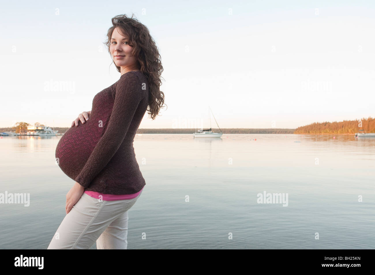 Femme enceinte avec les mains sur l'abdomen de patauger dans Clear Lake, Manitoba, Canada Banque D'Images