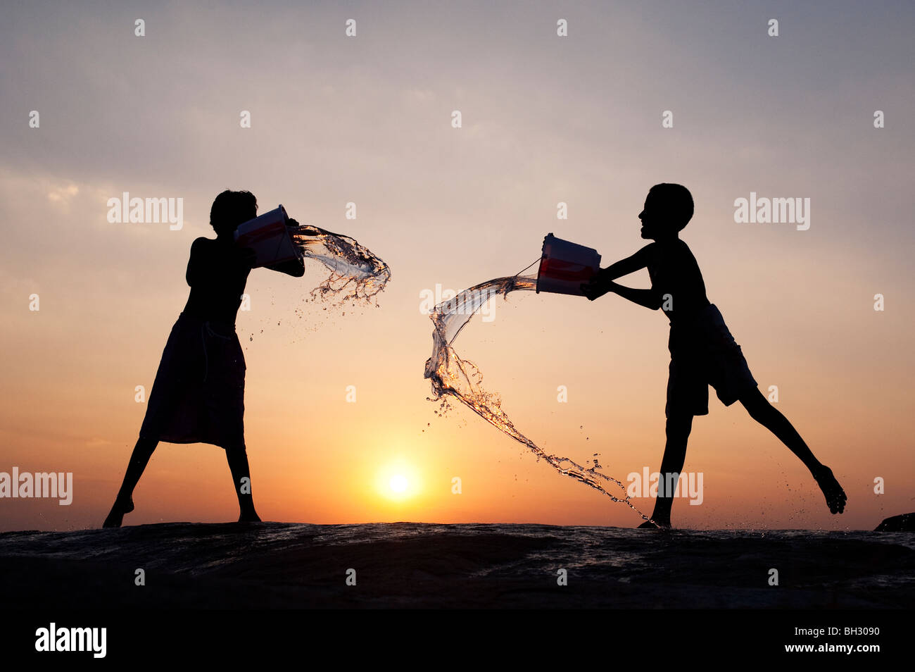 Les garçons indiens jetant de l'eau à chaque autres des seaux au coucher du soleil. L'Andhra Pradesh, Inde Banque D'Images