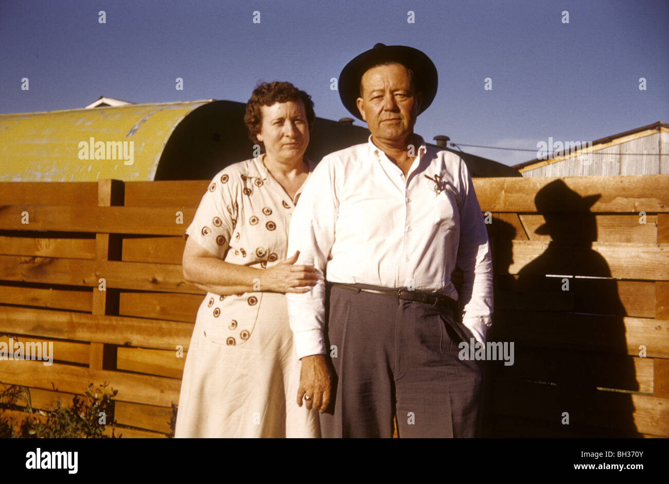 Vieux couple debout par une clôture dans l'Ouest américain pendant les années 50 ou 60. Banque D'Images