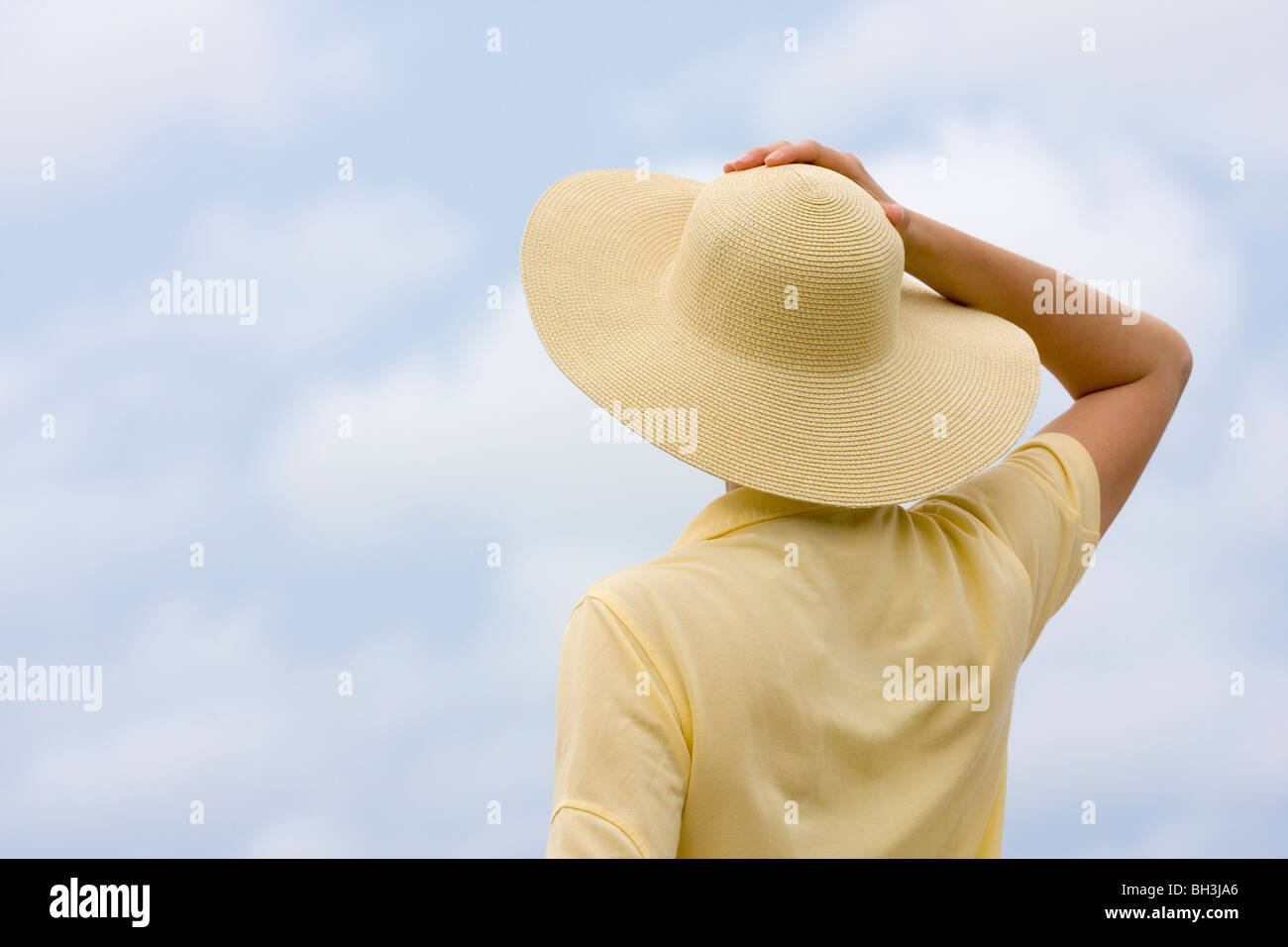 Womann jaune avec chapeau et chemise en face d'un ciel avec des nuages Banque D'Images