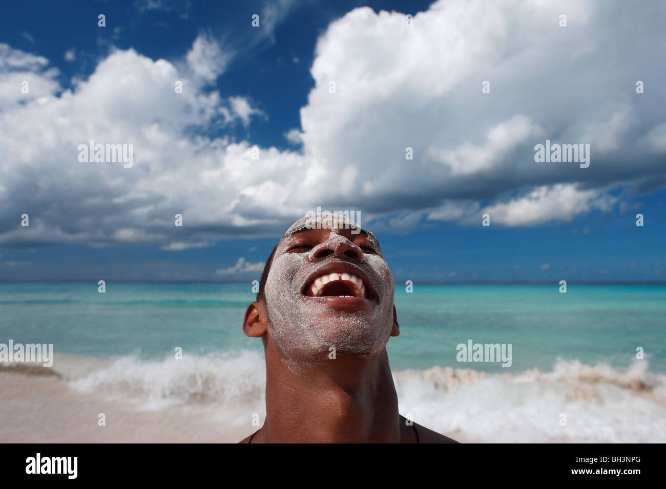 Jeune homme sur la plage avec du sable sur son visage, rire Banque D'Images