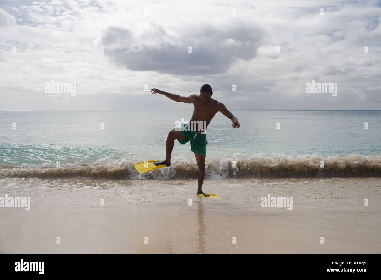 Jeune homme portant des palmes à pied de la mer sur une plage tropicale Banque D'Images