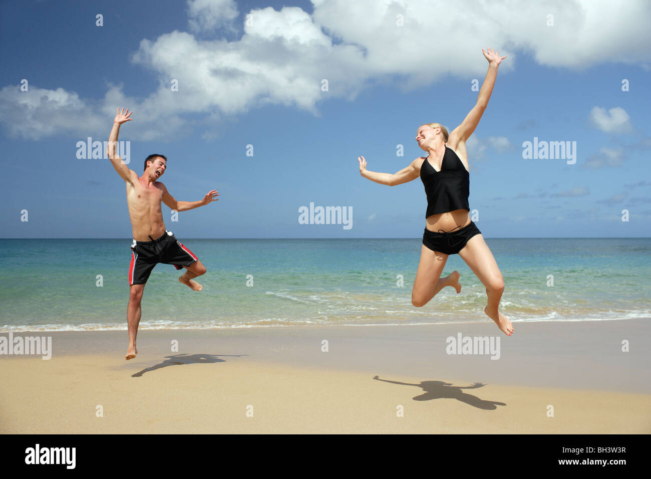 Jeune couple sautant sur une plage tropicale, rire Banque D'Images