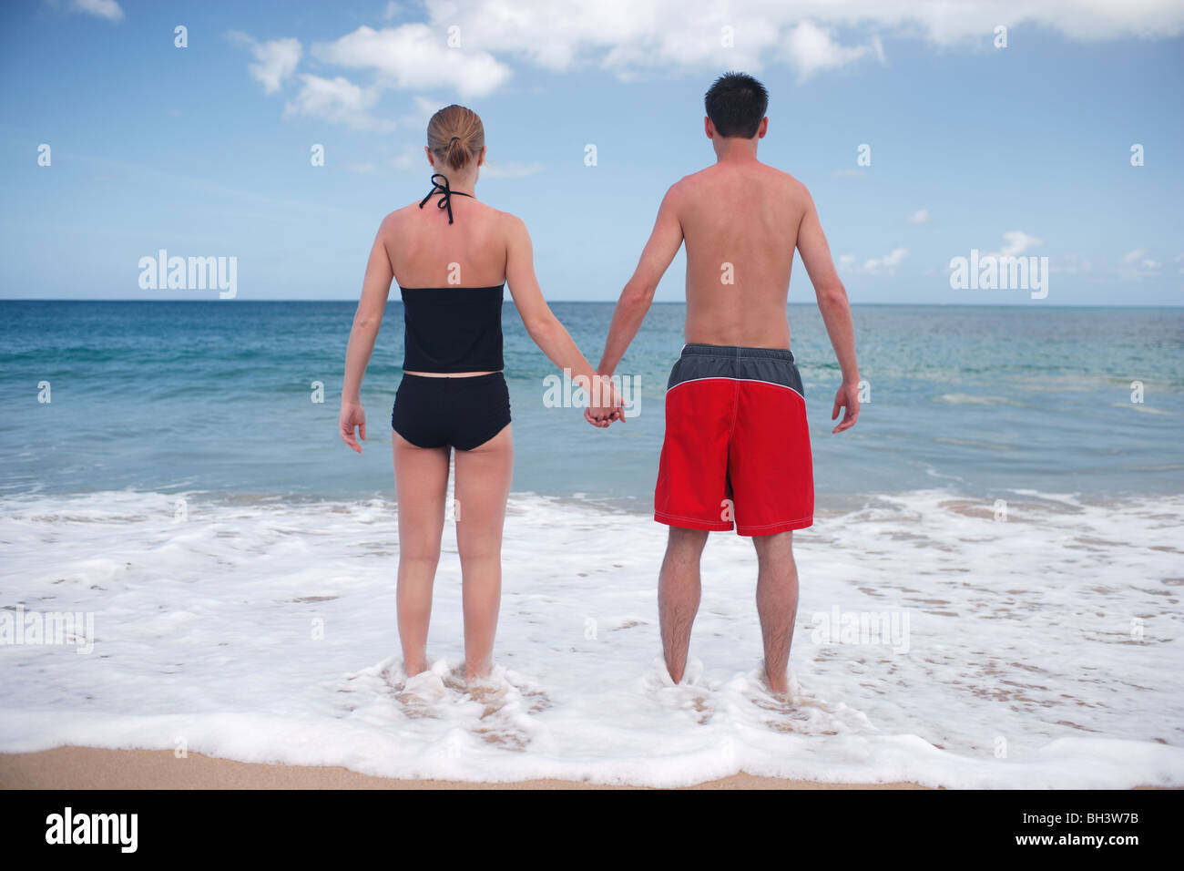 Young couple holding hands on beach à la recherche à l'horizon Banque D'Images