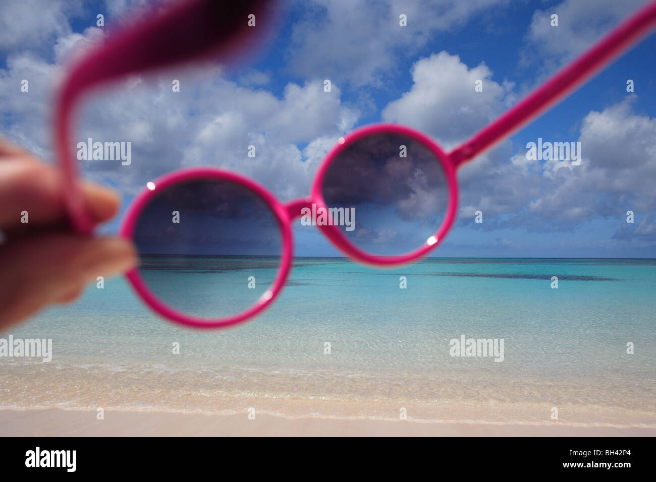 Une paire de lunettes roses détenues contre une scène de plage tropicale Banque D'Images