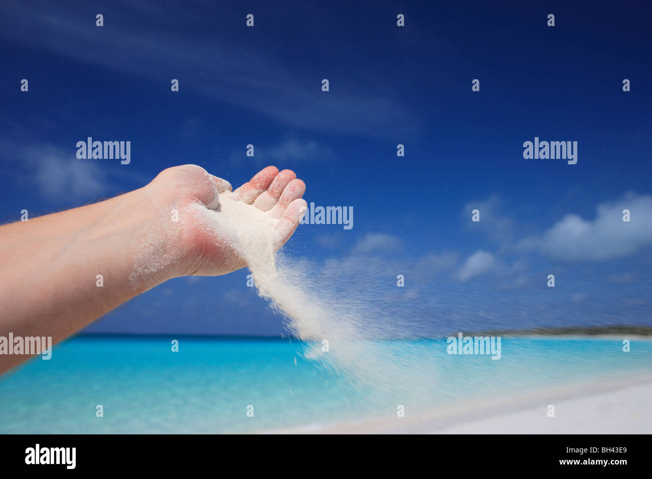 La main d'un homme versant le sable pris dans la brise sur une plage tropicale déserte Banque D'Images