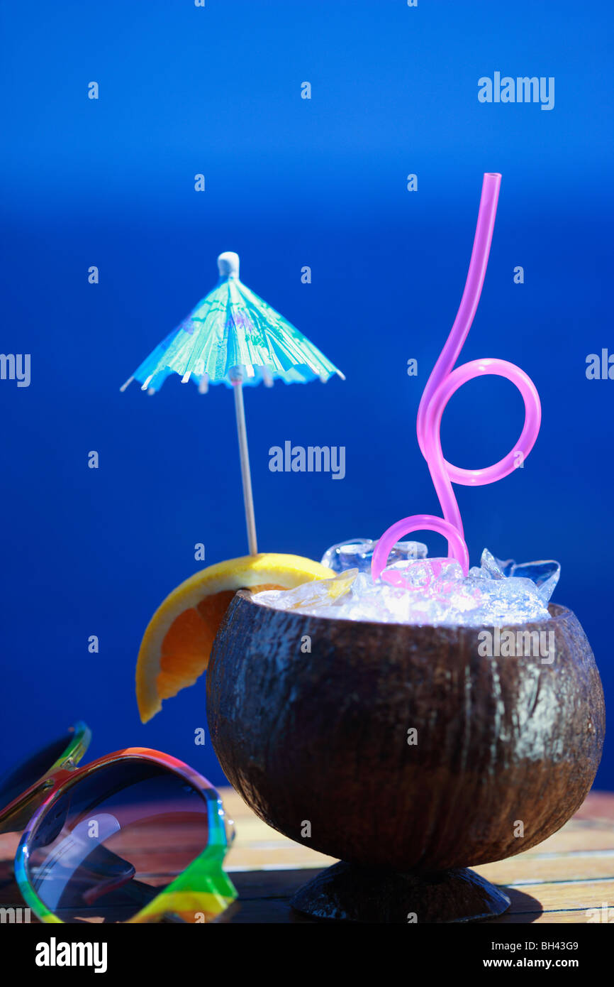 Un cocktail tropical dans une coque de noix de coco et une paire de lunettes de soleil contre un ciel d'été bleu Banque D'Images
