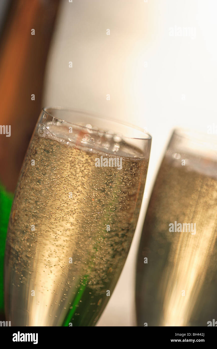 Close up of two champagne glasses plein de champagne et une bouteille de champagne à l'arrière-plan Banque D'Images