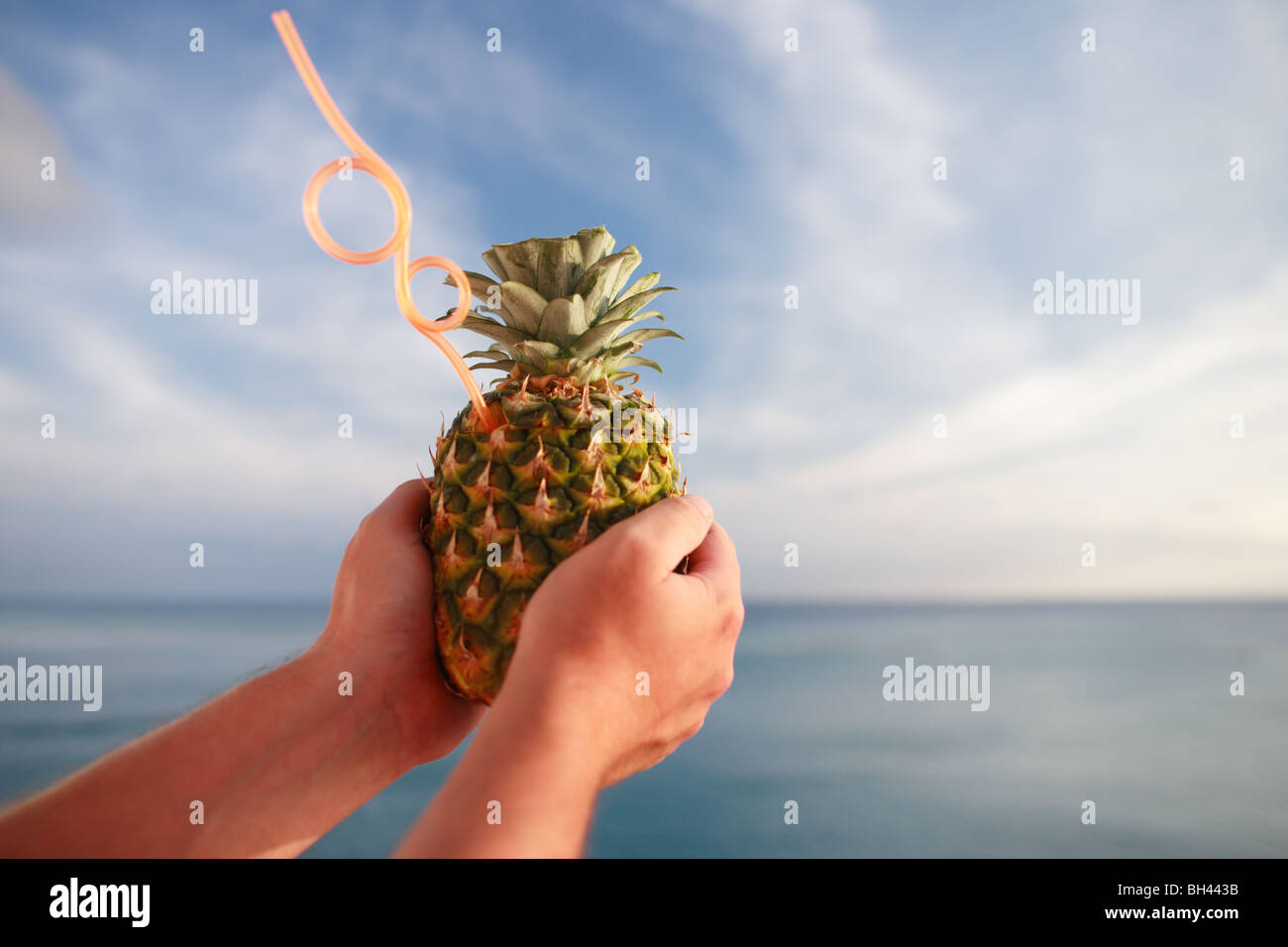 A man's hands holding un cocktail d'ananas tropical boire avec une paille contre une mer bleue et le ciel Banque D'Images