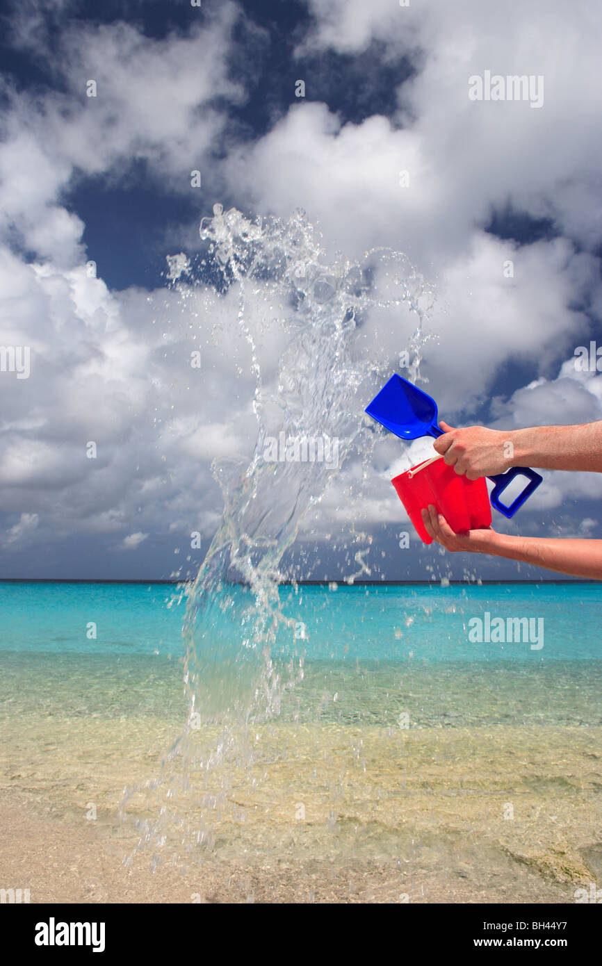 Les mains d'un homme jetant un jouet pour enfant et la cosse du godet plein d'eau dans l'air sur une plage tropicale déserte Banque D'Images