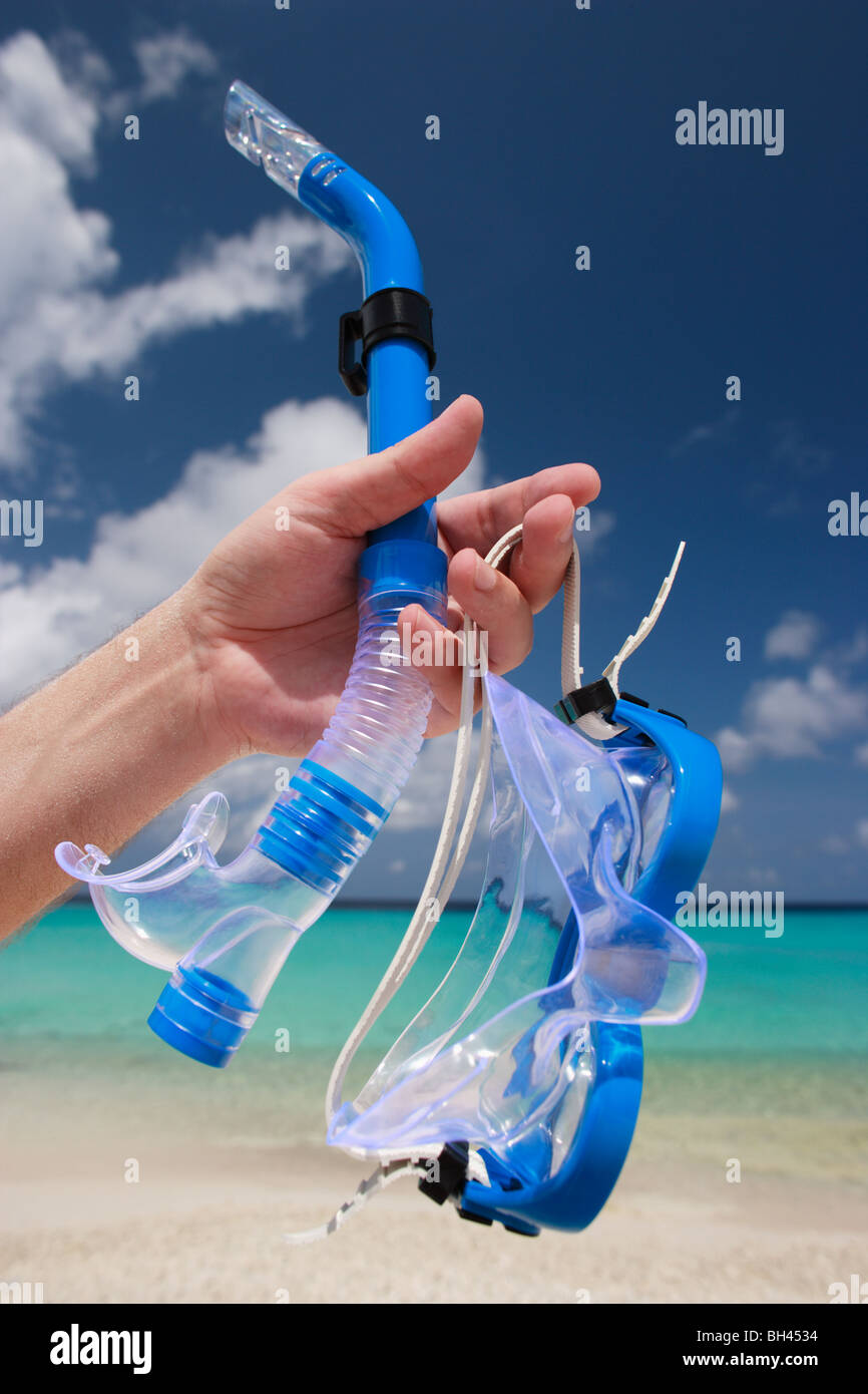 La main d'un homme tenant un masque et tuba bleu dans l'air sur une plage tropicale déserte Banque D'Images