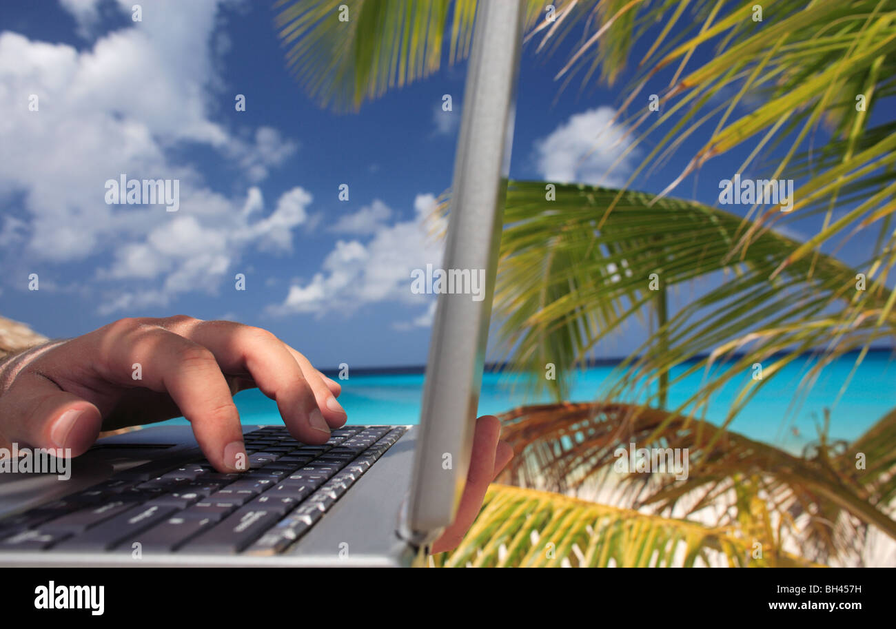 La main d'un homme à l'aide d'un ordinateur portable sur une plage tropicale Banque D'Images