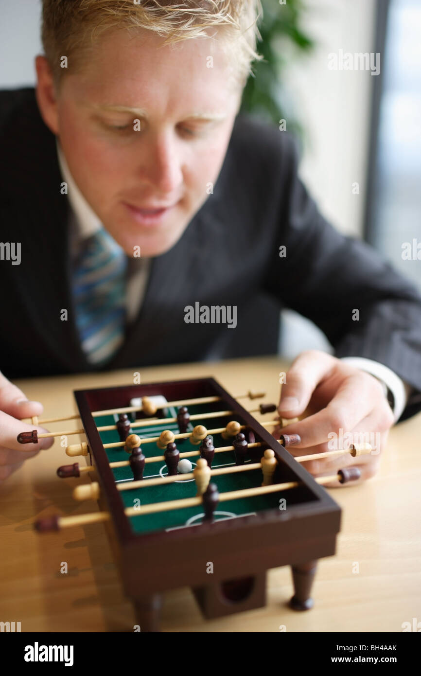 Un businessman playing miniature baby-foot at office desk,smiling Banque D'Images