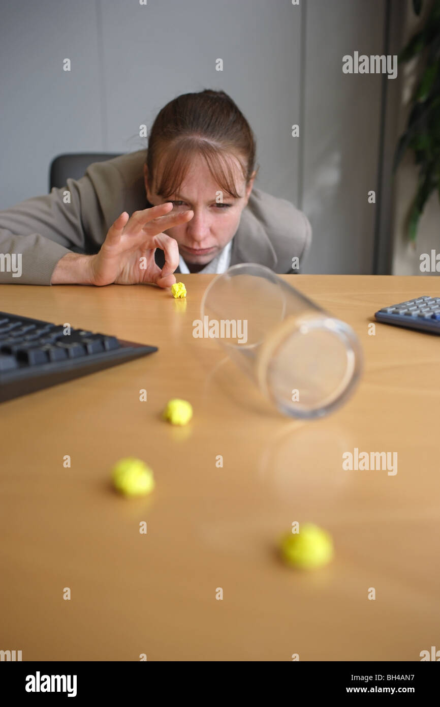Une femme sur le point d'une pichenette dans football papier un verre vide sur un bureau bureau avec une expression grave Banque D'Images