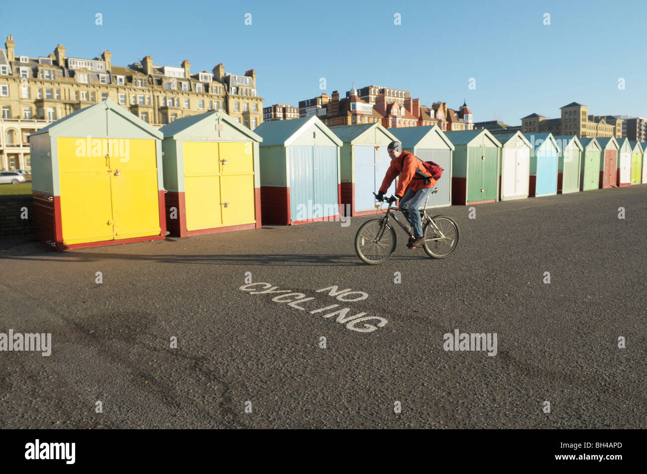 Un cycliste, équitation son vélo sur le front de mer de Brighton et Hove passé les cabanes de plage et d'un ''sign pas de vélo Banque D'Images