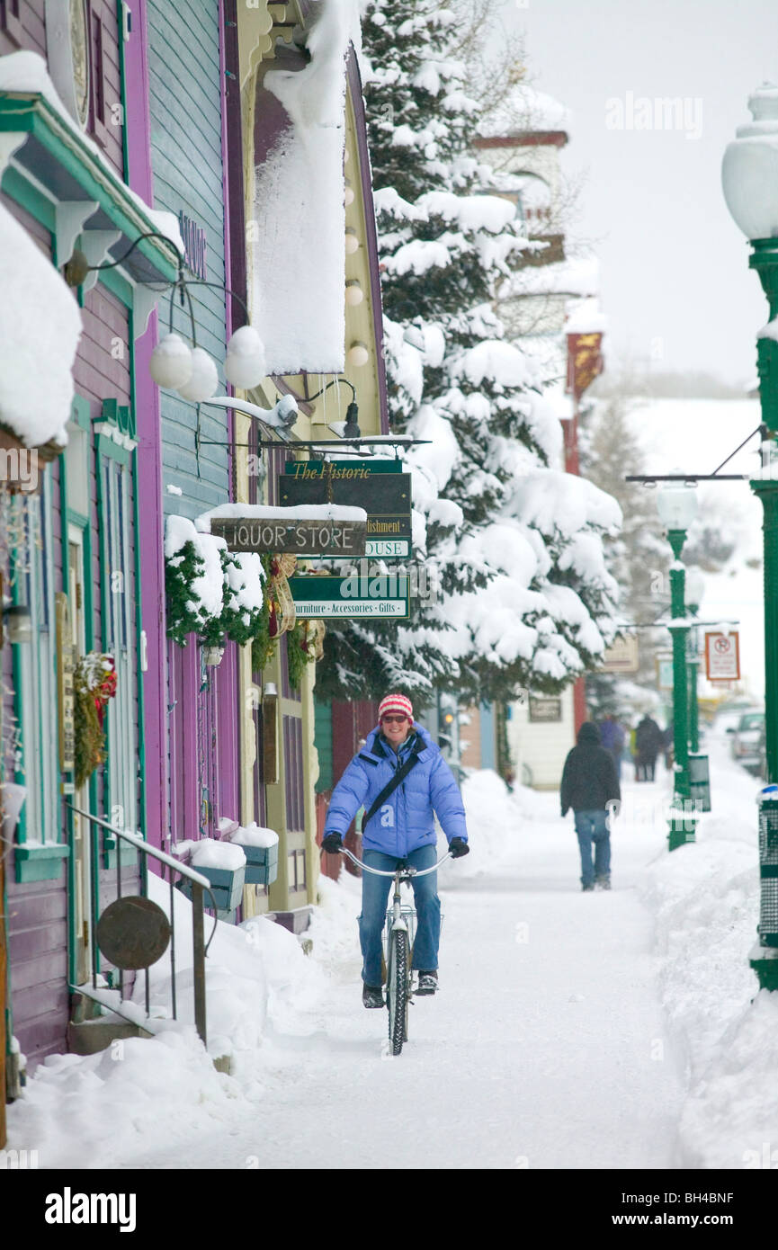 Woman riding a bike couvertes de neige vers le bas de l'Avenue Elk, Crested Butte, Colorado. Banque D'Images