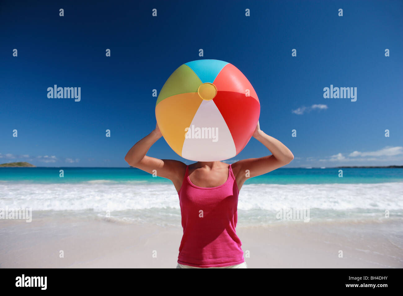 Jeune femme tenant un ballon de plage gonflable sur son visage sur une plage tropicale déserte Banque D'Images