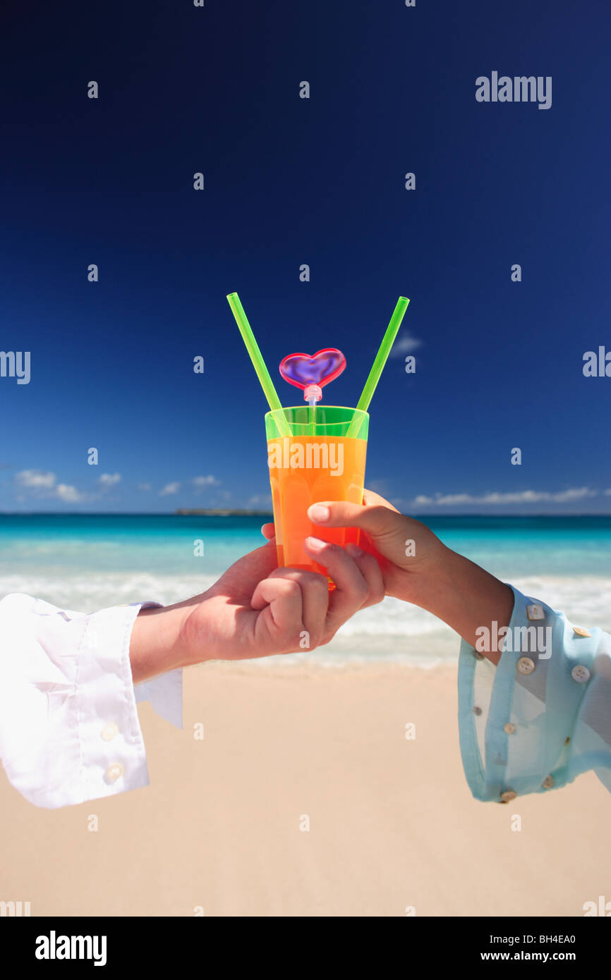 Jeune couple tenant un seul cocktail tropical sur une plage tropicale déserte Banque D'Images